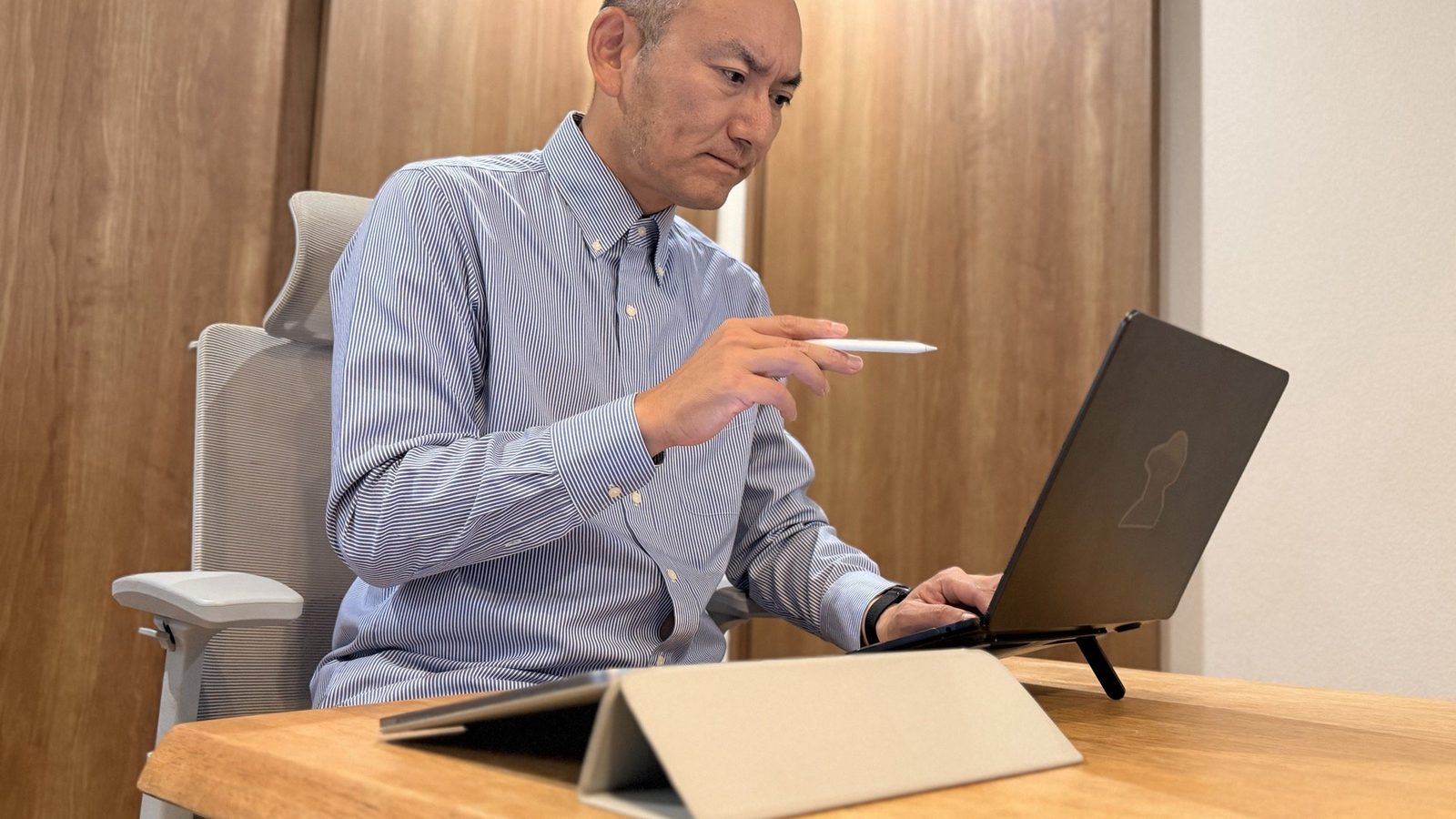 シャツ姿で、ノートパソコンに向かっているところ